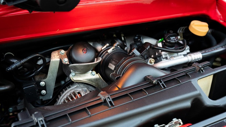 A close-up technical view inside a modern water-cooled flat-6 in the 1999 911 GT3, emphasizing the tight packaging of the black composite air intake system