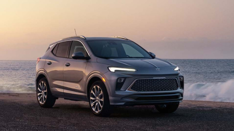 Front three-quarters shot of a silver Encore GX parked on the beach in front of crashing waves at dusk