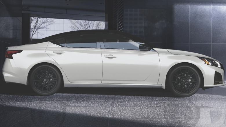 A side view of a white Altima parked on a glossy surface in front of a dark background