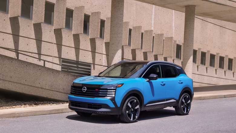 A Blue 2026 Nissan kicks parked in front of a geometric building.