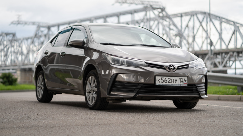 A Toyota Corolla parks near a bridge.