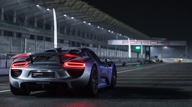 Porsche 918 Spyder on a racetrack at night, with a Porsche sign in the background.