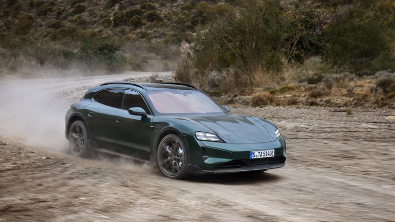 A dark green Porsche Taycan Turbo Cross Turismo kicking up dust while driving on an unpaved gravel trail, front three-quarter view.