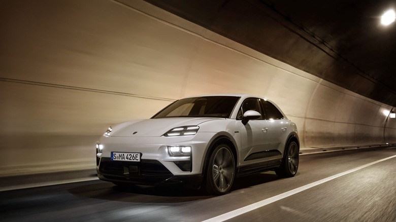 A white Porsche Macan Turbo Electric driving through a lighted tunnel, front three-quarter view.