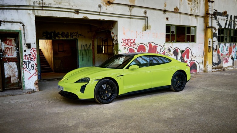 Acid Green Porsche Taycan GTS sedan parked in front of a graffiti-covered industrial building, front three-quarter view.