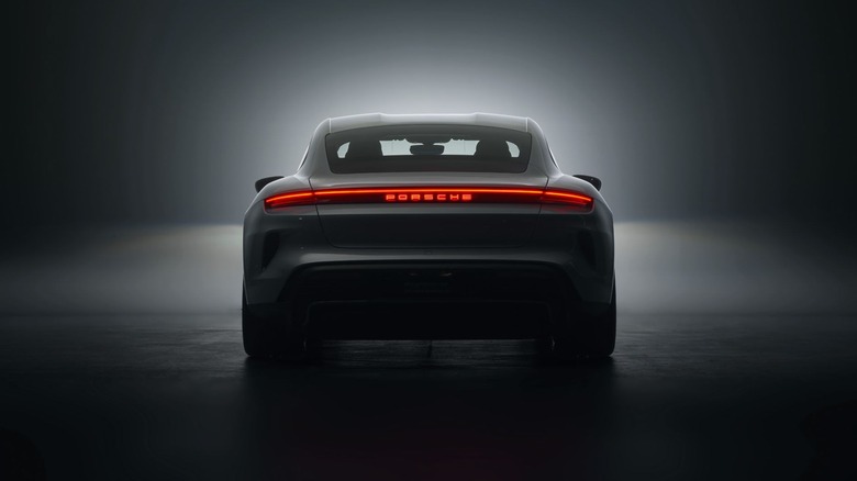 A Porsche Taycan Turbo S rear profile in a moody studio setting highlighting the illuminated full-width red LED lightbar.