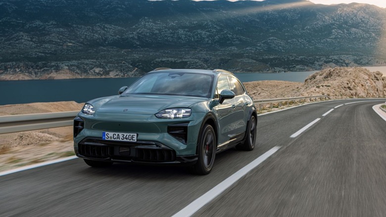 A Porsche Cayenne Turbo Electric SUV in slate green navigating a winding coastal mountain road, front three-quarter view.