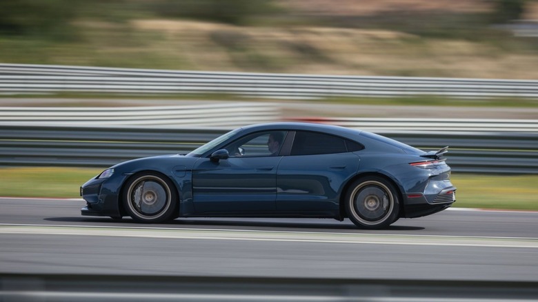 Porsche Taycan Turbo GT in metallic blue accelerating around a racetrack curve with deployed spoiler, side profile panning shot.