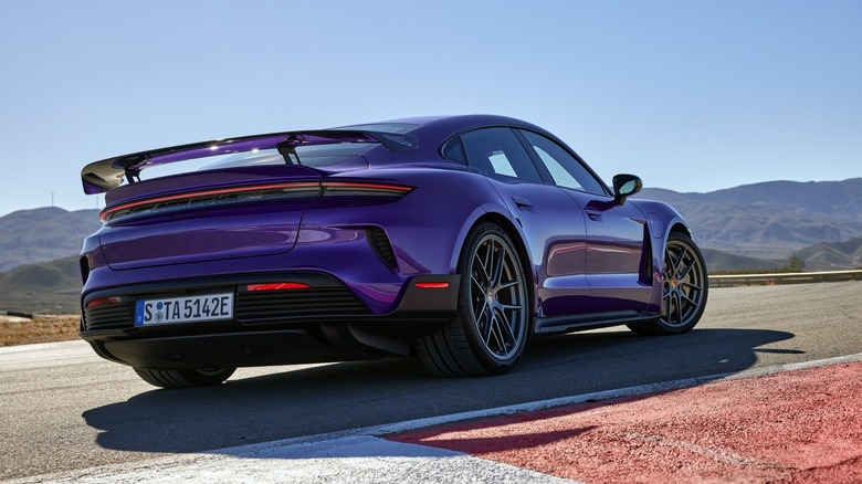 A low rear three-quarter track shot of a Porsche Taycan Turbo GT with Weissach Package in Purple Sky Metallic, highlighting the prominent fixed carbon-fiber rear wing.
