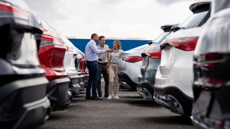 A car salesman showing a couple around a new car lot.