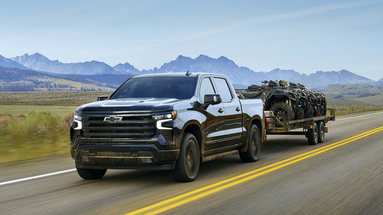 A black 2025 Chevrolet Silverado 1500 towing ATVs in a trailer on an open road