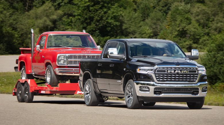 A black 2026 Ram 1500 towing an old red Dodge truck on an open road