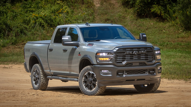 A grey 2026 Ram 2500 HD front 3/4 view on a dirt road with greenery in the background