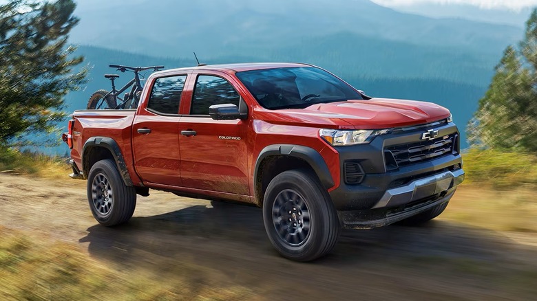 2025 Chevrolet Colorado driving on a dirt road with trees and mountains in the background