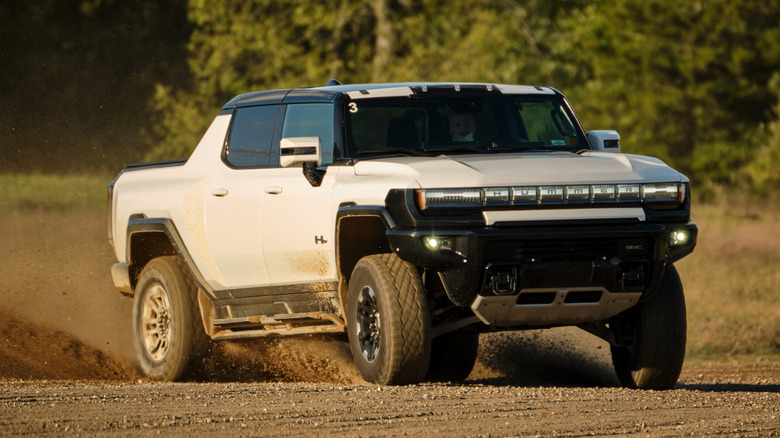 A white GMC Hummer EV Pickup plays and drifts sideways through gravel and dirt.