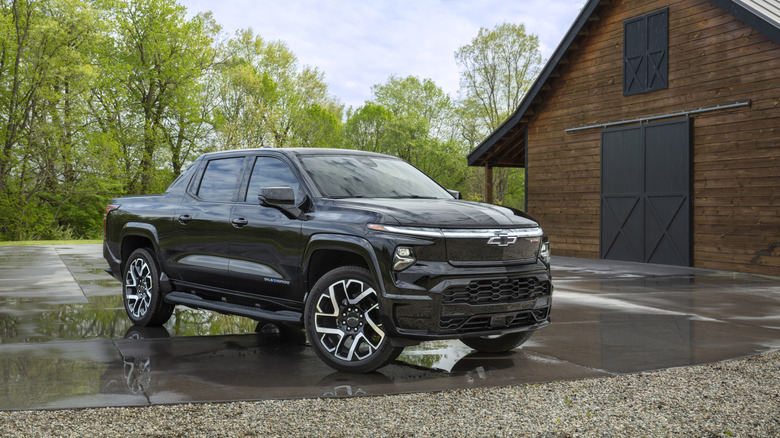 Black 2024 Chevy Silverado EV RST set in front of a barn background on a wet driveway.