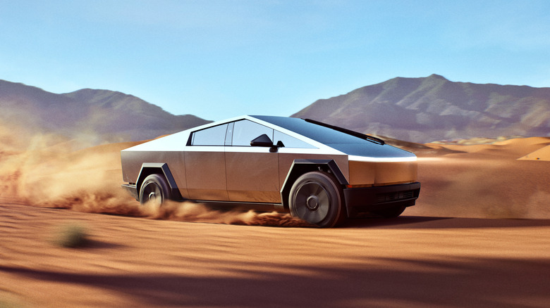 A Cybertruck traverses a dusty, sandy desert dune.