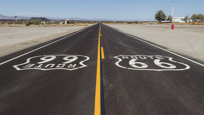 A road goes up the center of the image in a desert area, a shield-like stamp is on each side of the road, reading "Route 66"