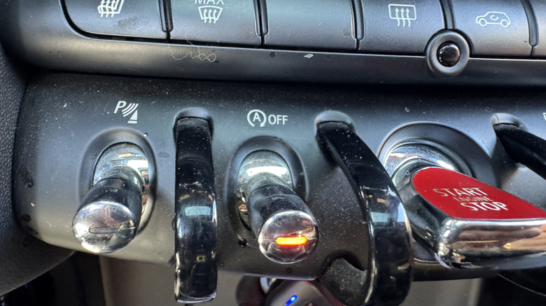 A close-up of the auto start/stop toggle in my Mini Cooper S with the tip illuminated orange signifying that I have the system turned off. Yes my dashboard was dusty when I took this photo, and yes I have dusted it since then.