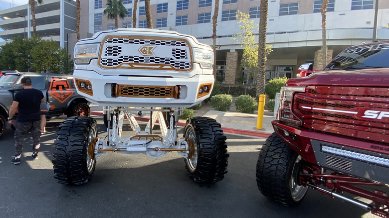 A head-on shot of a white and gold Dodge Ram HD that's been lifted by several feet on display at SEMA