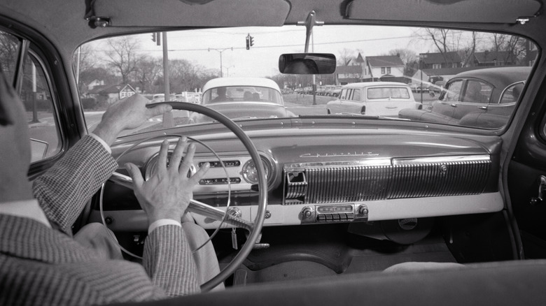 1950s Back View Impatient Man Driving Honking Horn On Steering Wheel Scene Of Traffic Out The Front Windshield Chevrolet Logo.