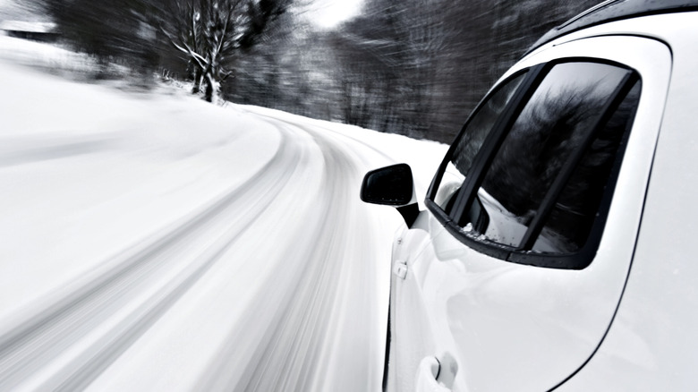 Left broadside of achromatic SUV driving connected snowy road