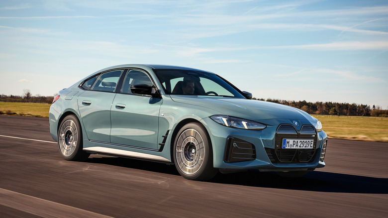 Front three quarters shot of a blueish BMW i4 driving in front of grass