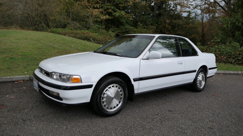 front three quarters view of a white Honda Accord Coupe parked on asphalt next to a grass hill and trees behind it
