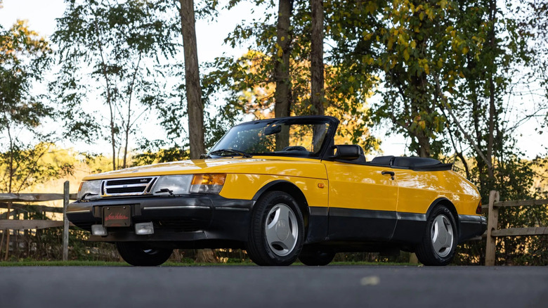 front three quarters shot of a yellow Saab 900 Turbo cabriolet with its top down parked under trees