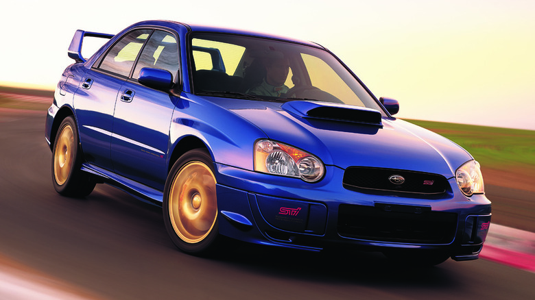 front three-quarters shot of a blue and gold blob-eye WRX STI driving around a corner on a racetrack