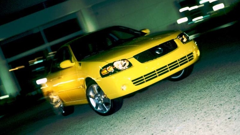 front three quarters shot of a yellow Sentra SE-R driving at night in front of ta building