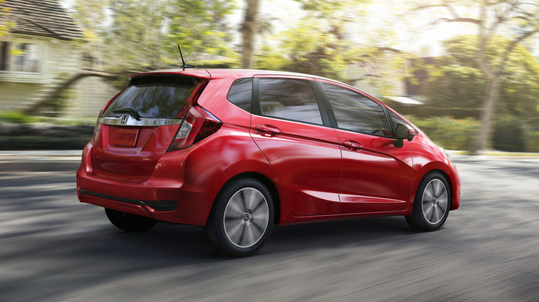 rear three quarter shot of a red Honda Fit driving down a tree-lined residential street