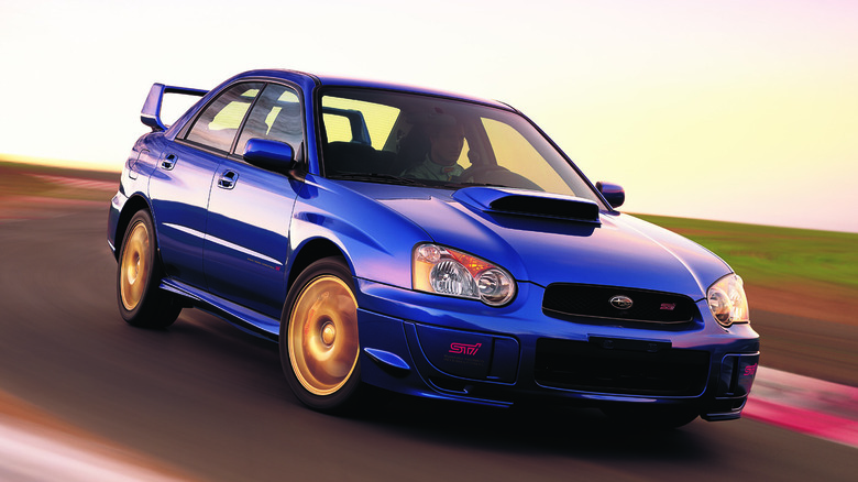 Front three quarters shot of a blue and gold blob-eye WRX STI driving around the corner on a racetrack