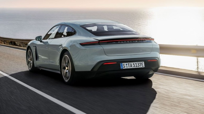 rear three-quarters shot of a light colored Taycan driving on a coastal road at sunset