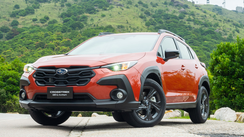 An orange Subaru Crosstrek sitting parked near a hill.