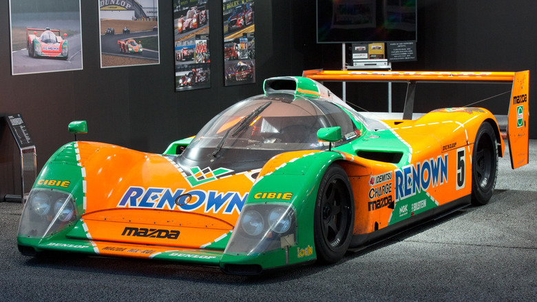 The bright orange and green liveried Mazda 787B Renown captured in a museum setting.