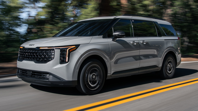 2025 Kia Carnival Hybrid driving down a road with double yellow lines painted in the middle