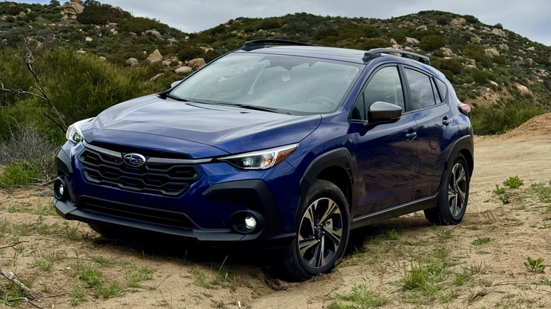 front three quarters shot of a blue Subaru Crosstrek parked on dirt in front of a rocky hill