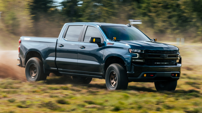 Blue 2024 Chevrolet Silverado Z71 pickup truck front right view seen driving in a field
