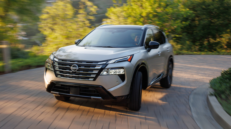 Tan 2024 Nissan Rogue SUV front left view seen driving on a brick raod