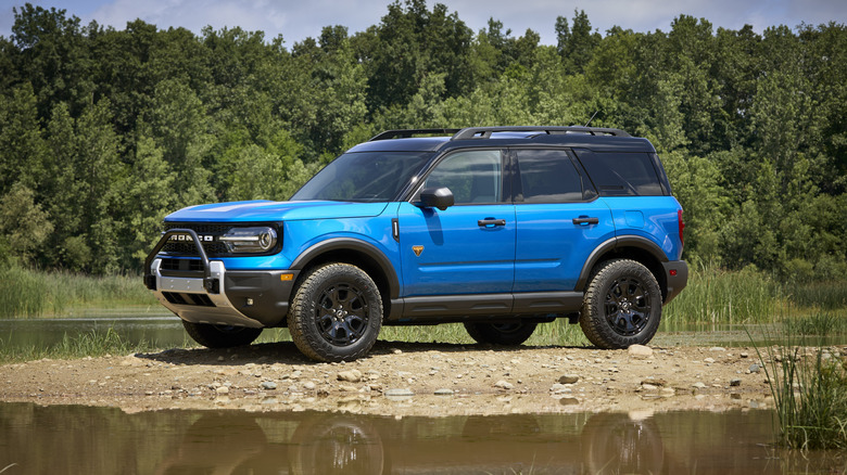 A blue Ford Bronco Sport parked on rocky terrain in front of water.