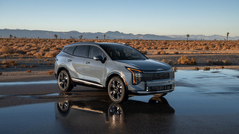 A gray 2026 Kia Sportage HEV parked on a wet road in a desert environment.