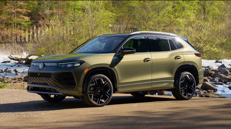 A green 2026 Volkswagen Tiguan parked on a dirt road with a mountain stream in the background.