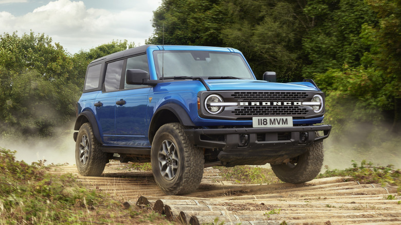 A blue Ford Bronco parked on a dirt road in front of trees