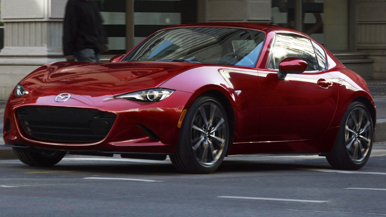 Red 2026 Mazda MX-5 Miata driving down a city street.