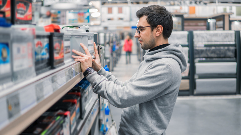 Man looking at car batteries on a shelf in a store.