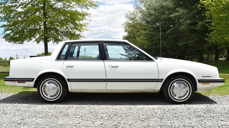 A white 1984 Chevrolet Celebrity  parked on a gravel surface.