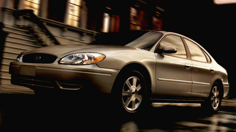 Catalogue photo of a beige 2004 Ford Taurus moving on a street in front of brownstone apartments.