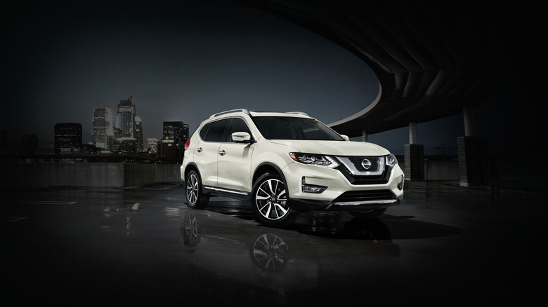 A white 2020 Nissan Rogue on a dark parking bridge with a dark cityscape behind it in the distance.