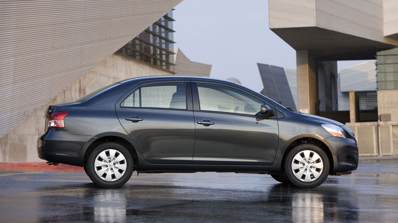 A dark grey 2009 Toyota Yaris sedan in an office building parking lot area.